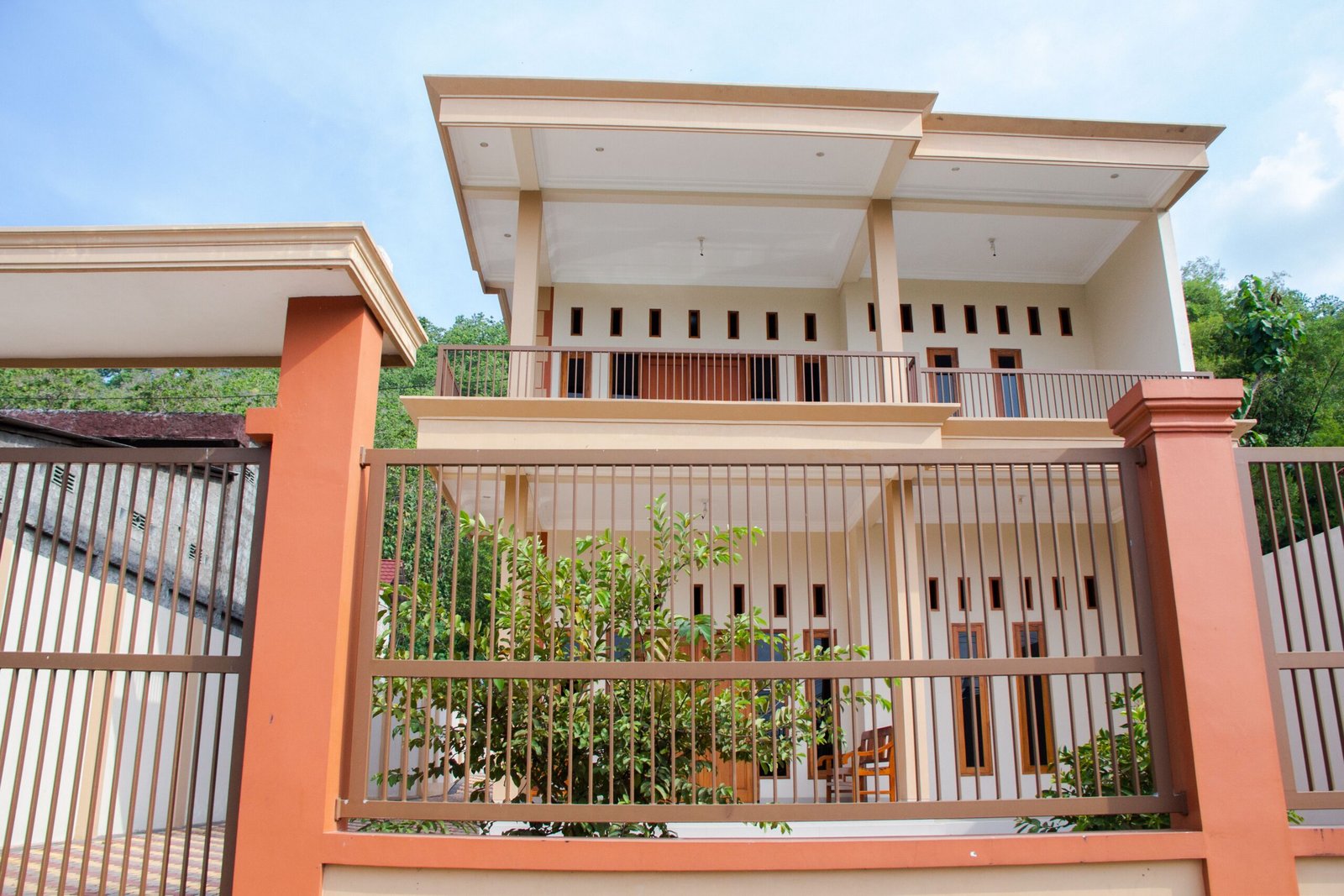 Low angle view of a modern two-story residential house with a balcony and fenced yard.